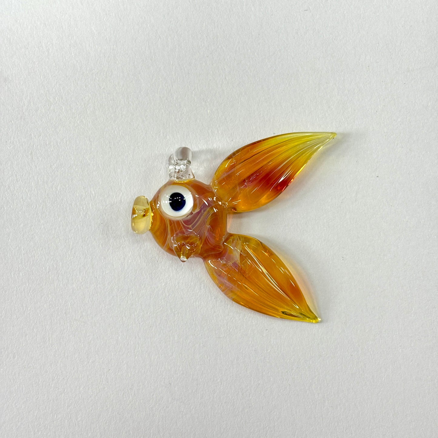 Glass fish ornament, in the borosilicate color Amber Purple on a white background